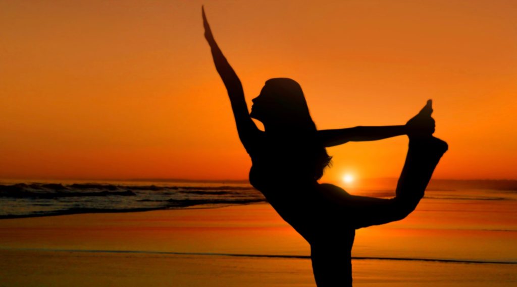 Healthy young woman practicing yoga at sunset on the beach