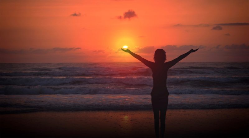 Celebrating life - A woman raises her arms at sunset on a deserted beach